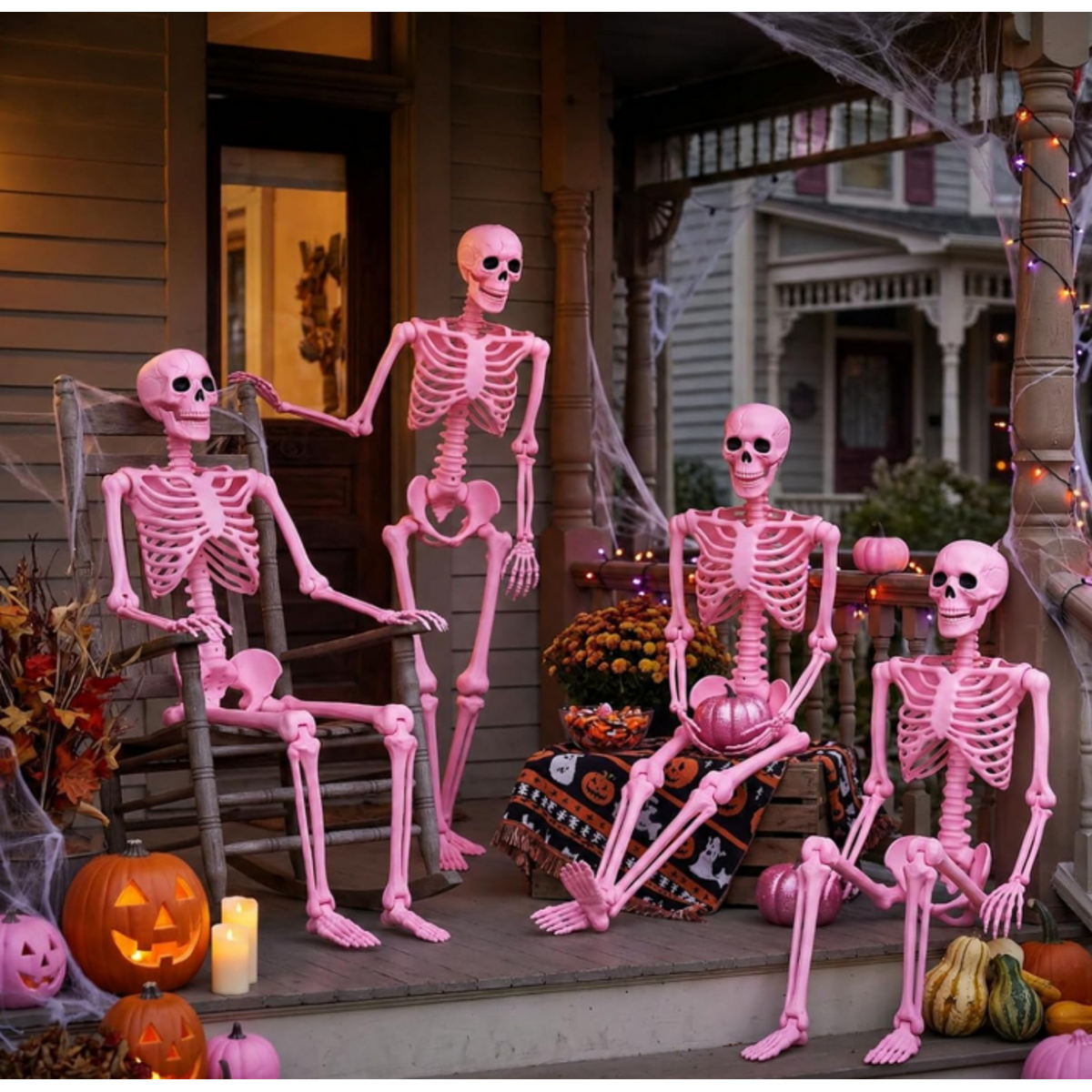 Four pink skeletons posed on a decorated Halloween porch.